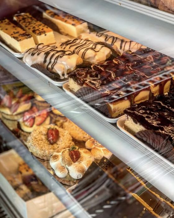 Angled shelves of the display cabinet holding eclairs, chocolate-drizzled slices and cheesecake.