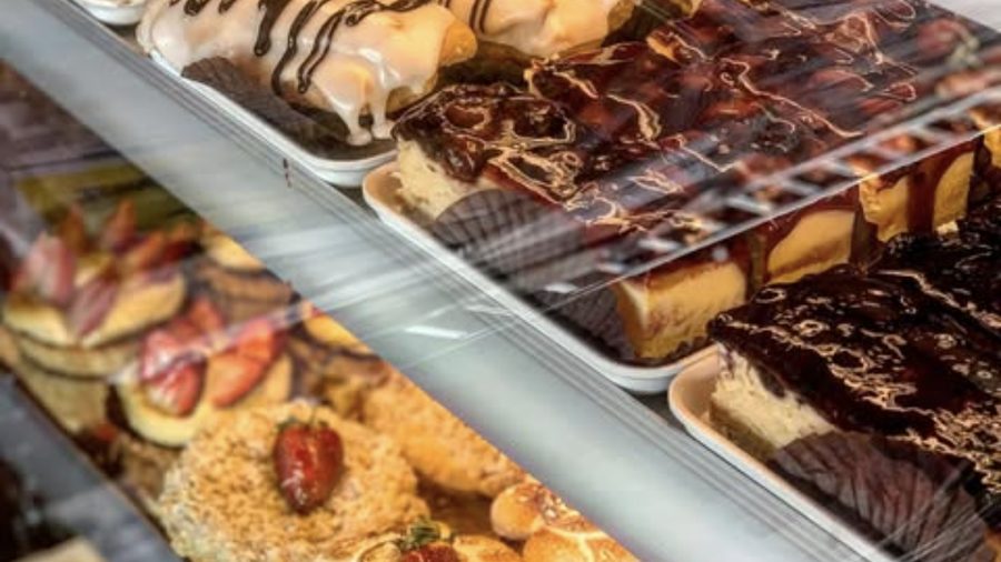 Angled shelves inside the display cabinet, filled with eclairs, chocolate-topped slices and cheesecake under warm light.