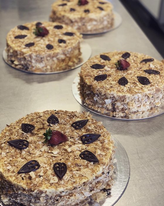 Three round Napoleon torts coated in pastry crumb, each topped with a strawberry and hand-piped chocolate leaves.
