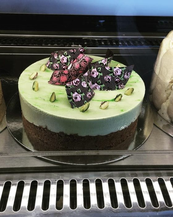 A pistachio mousse cake on a chocolate base, decorated with patterned chocolate shards and whole pistachios.