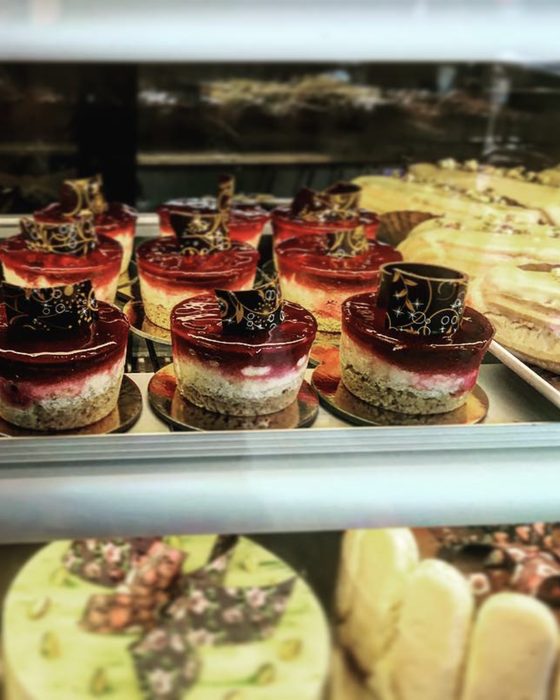 A tray of individual raspberry cheesecakes with glossy red tops and printed chocolate collars.