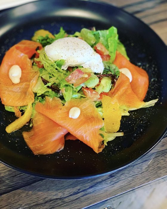 Smoked salmon folded over a citrus salad with a poached egg on top, on a black plate.